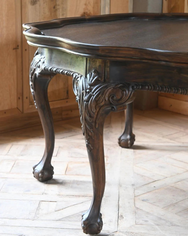 Cabriole leg center table shown close-up at one curved leg, with carved detailing beneath the dark tabletop.