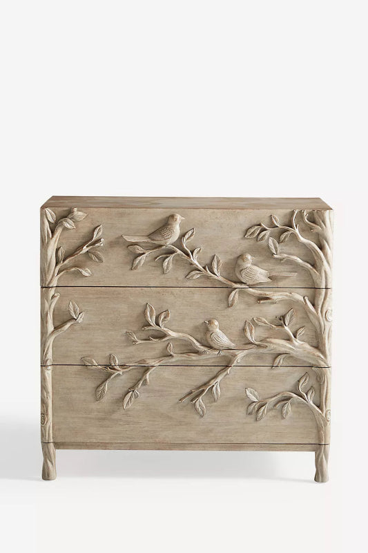 Three-drawer wood chest with hand-carved birds and leafy branches flowing across its washed-grey front.