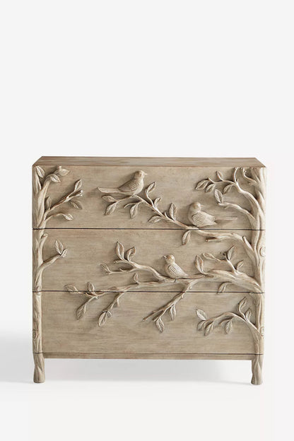 Three-drawer wood chest with hand-carved birds and leafy branches flowing across its washed-grey front.