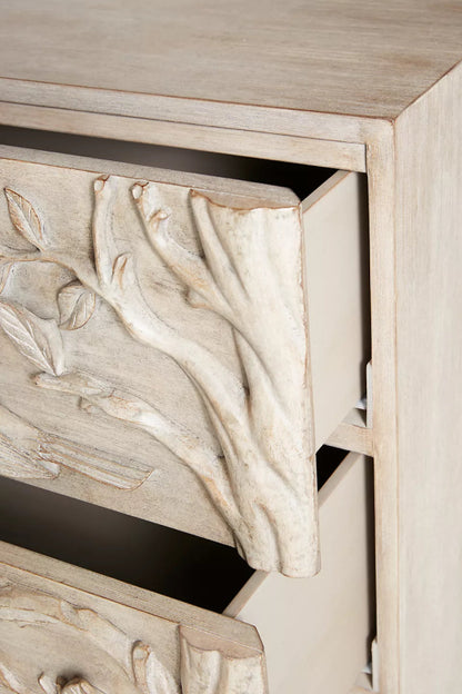 Close-up of the washed-grey wood dresser, showing hand-carved birds and leafy branches on its drawer front.