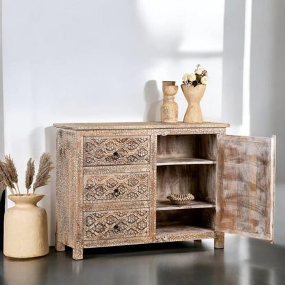 Carved cabinet buffet with a pale distressed finish, styled against a wall with its right-hand cabinet door open.