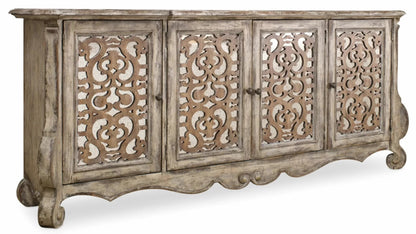 Straight-on against a pale background, the distressed white server shows carved scrollwork across its four doors