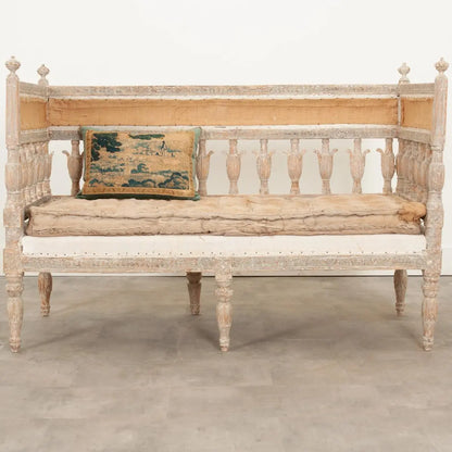 Carved hall bench in pale wood with a cushioned seat, front view showing its open slatted back and turned legs.