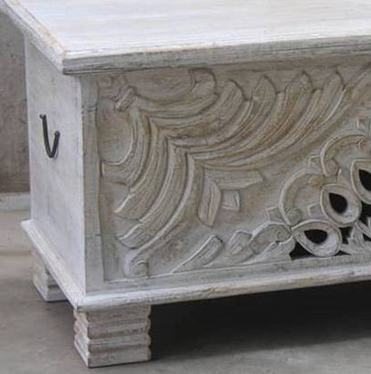 Rustic carved storage trunk in solid wood, corner detail view showing sweeping relief carving and a dark side handle.