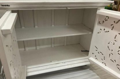 Carved white storage cabinet in a side profile view, showing its depth, flat top and lower support.