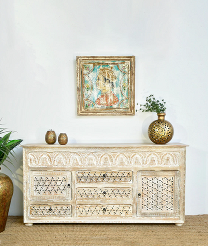 Carved white wood sideboard with patterned doors and drawers, shown straight on against a pale wall with decor.