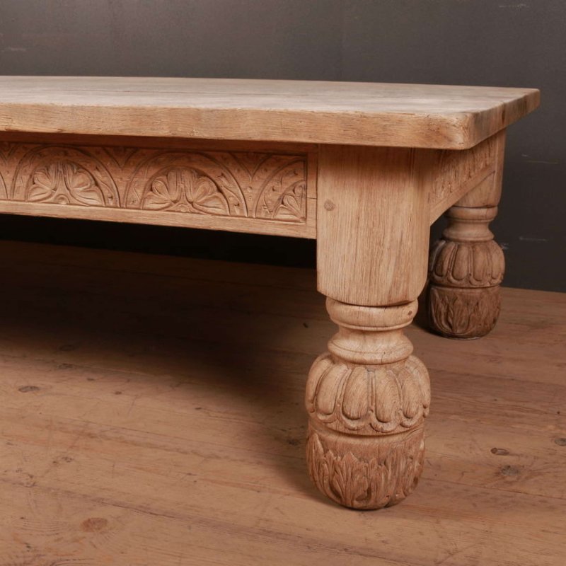 Carved wood center table with a pale top and sculpted front leg, seen from a low front angle on a wood floor.