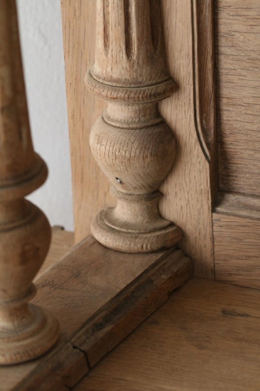 Carved wood china cabinet with a lower corner and shaped foot, close-up beside a pale wall and floor.