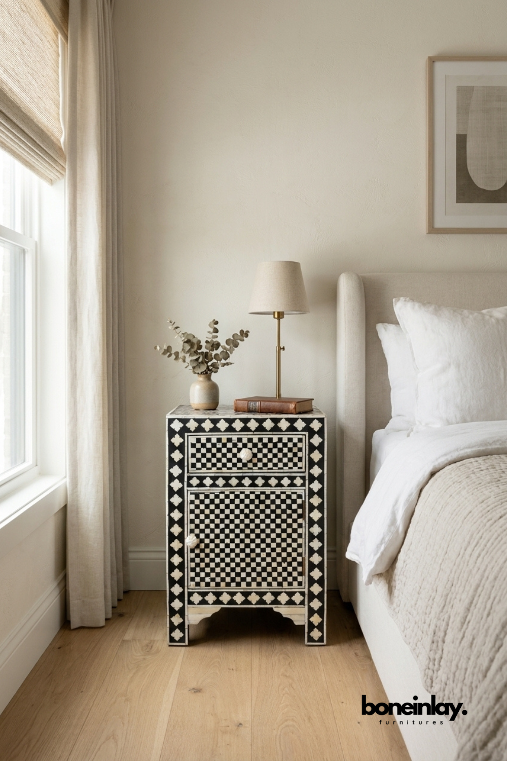 Black and white checkerboard bone inlay nightstand with drawer and cabinet door styled beside a bed in a neutral bedroom setting with lamp and eucalyptus decor