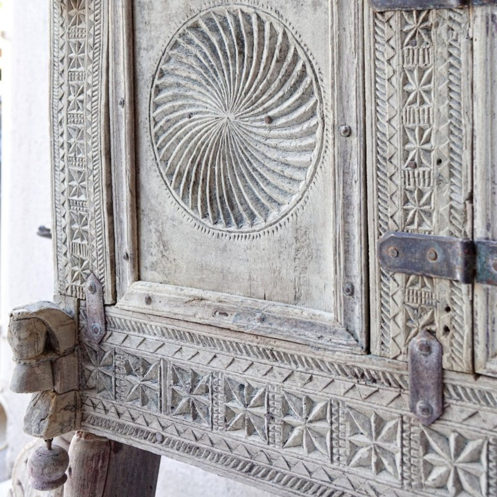 Circular-carved wooden hope chest in a weathered finish, corner detail view showing spiral relief and metal hinges.