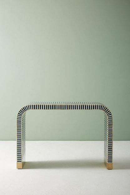 Front angle of the blue bone inlay console table, showing the curved waterfall silhouette, linear stripe pattern across the face and top, and brass-capped feet. The portrait product view keeps the handmade entryway table centered for clear visibility of its blue finish.