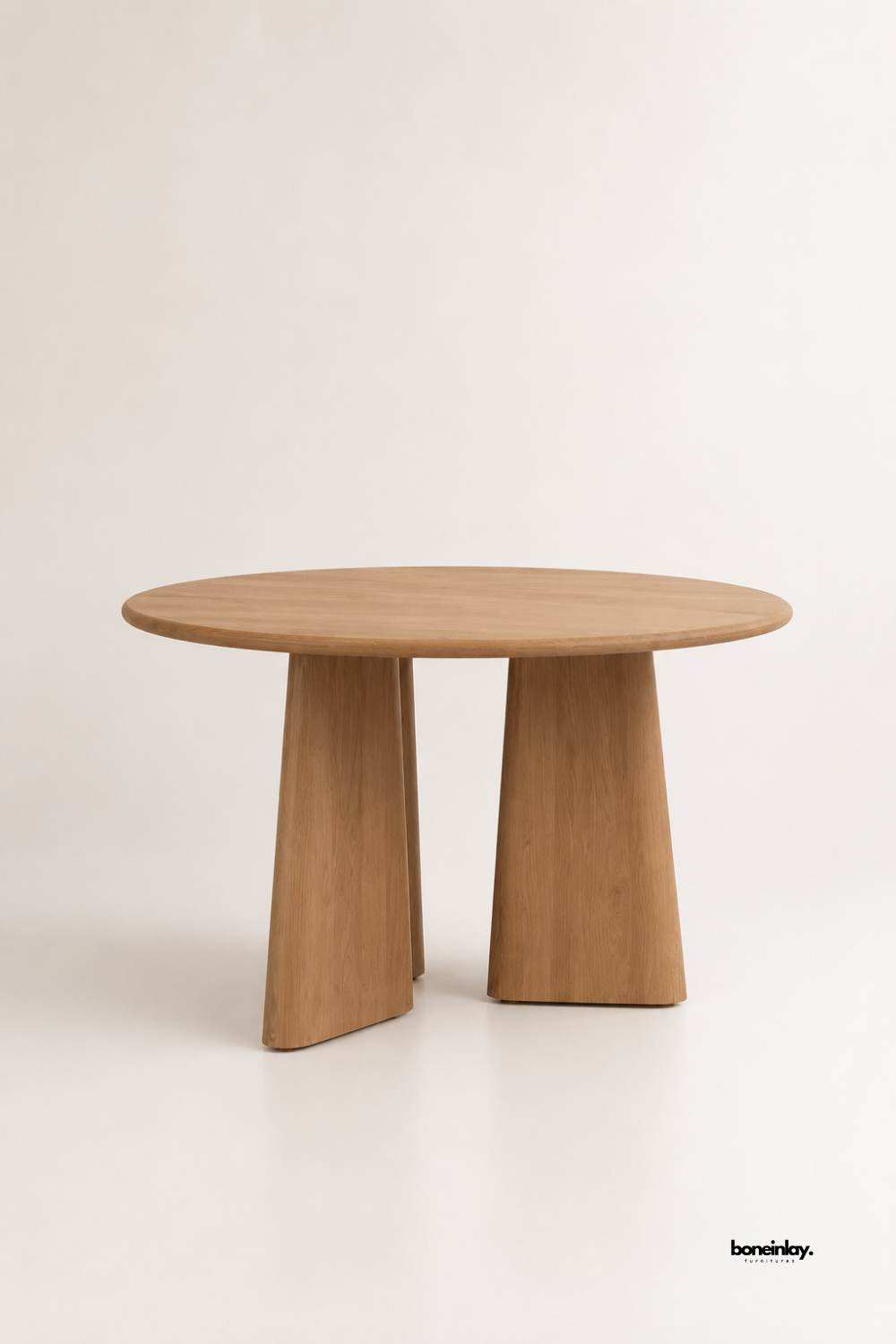 Artisan-crafted solid light oak round dining table showcasing sculptural angled pedestal base legs and clean circular contours against a clean studio backdrop. This contemporary wooden dining and breakfast table offers timeless minimalist aesthetics, durable craftsmanship, and organic warmth for modern interiors.