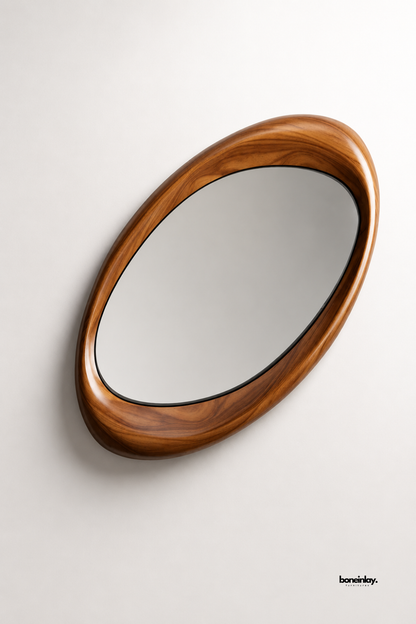 Artisan-crafted organic oval wooden frame mirror featuring a smooth sculpted profile and polished warm walnut finish displayed on a clean studio background. This contemporary asymmetrical wall mirror functions as both a statement art piece and a functional vanity mirror for modern entryway or bedroom decor.