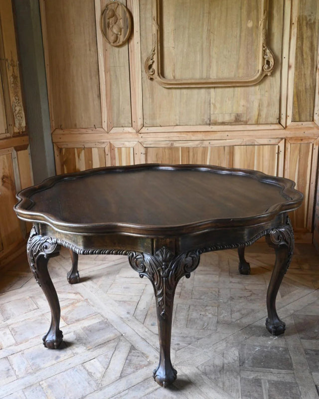 Curved leg coffee table in a front view, with its round dark top, shaped apron and legs visible against the wall.