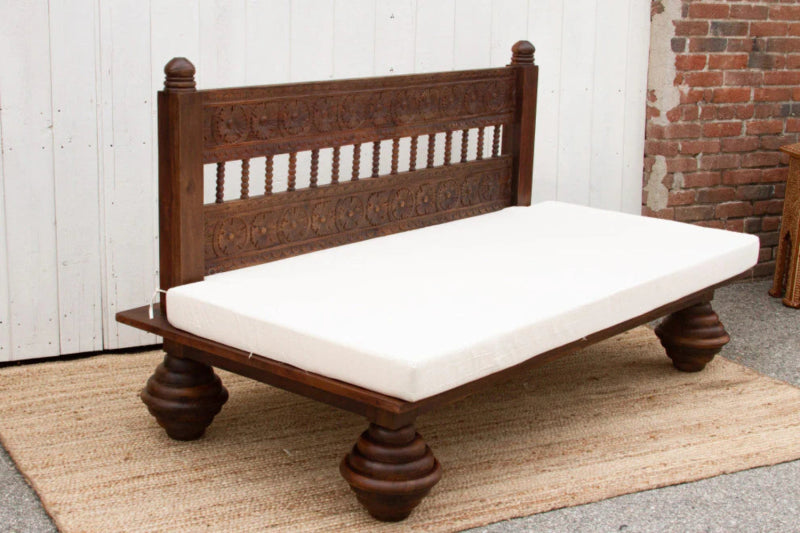 Dark wood daybed bench with a slatted back and white cushion, shown from the side with its rounded feet visible.