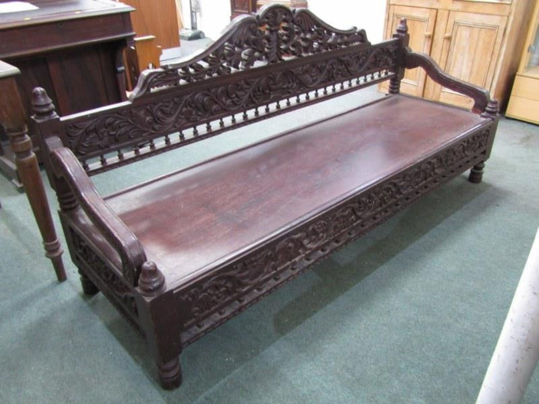 A grand solid wood daybed bench with a deep dark finish, featuring an intricately hand-carved floral backrest and apron in a traditional architectural style.