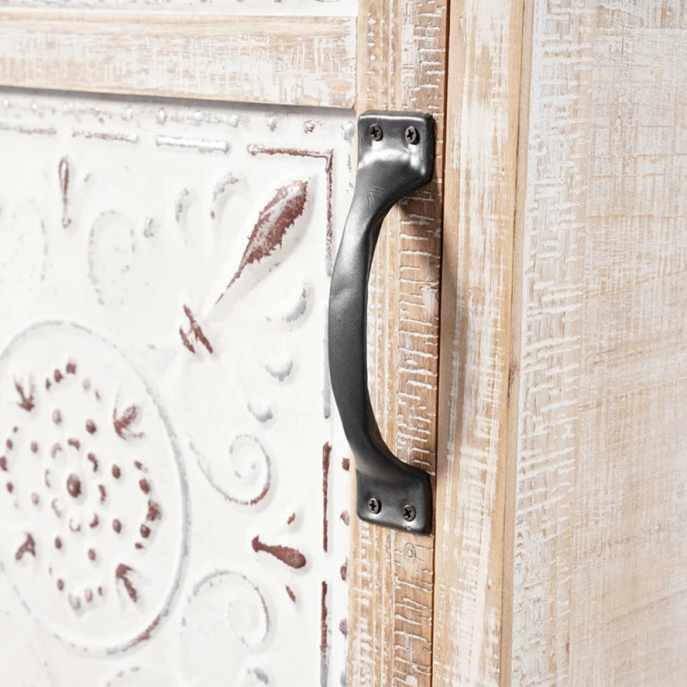 Distressed white cupboard, close-up of the drawer handle beside the raised floral carving on its pale door.