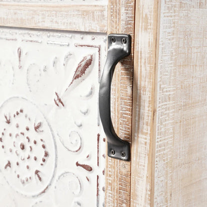 Distressed white cupboard, close-up of the drawer handle beside the raised floral carving on its pale door.