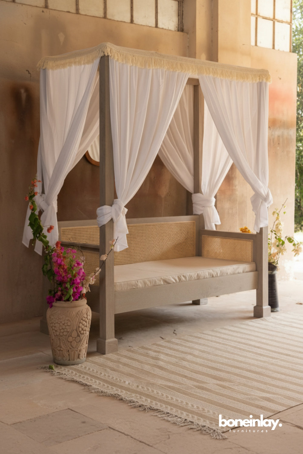 Canopy daybed with sheer white drapes and cane detailing styled in a warm indoor-outdoor setting.