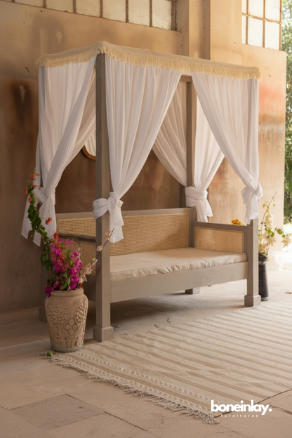 Canopy daybed with sheer white drapes and cane detailing styled in a warm indoor-outdoor setting.