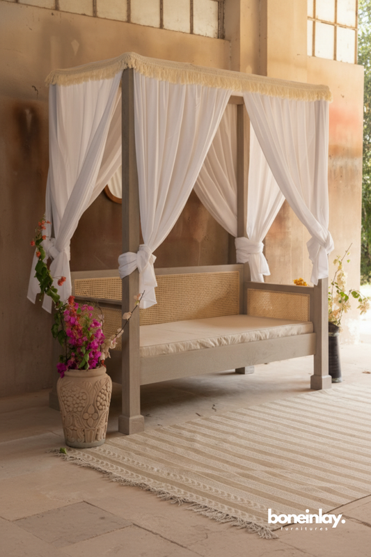 Canopy daybed with sheer white drapes and cane detailing styled in a warm indoor-outdoor setting.