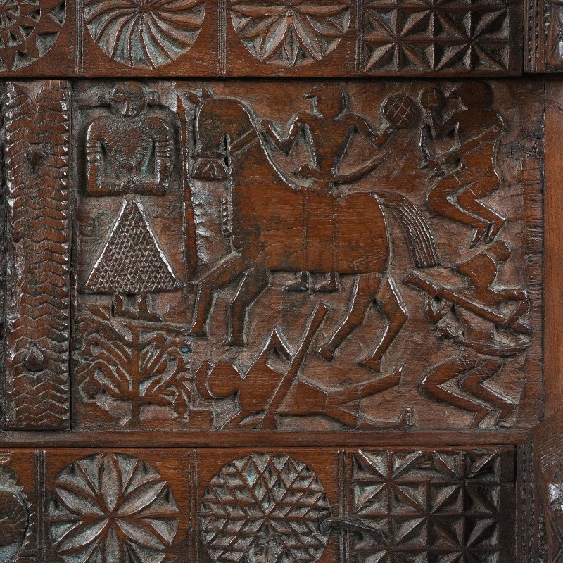 Figural carved hope chest in natural solid wood, front view close-up showing a horse, human figures and floral borders.