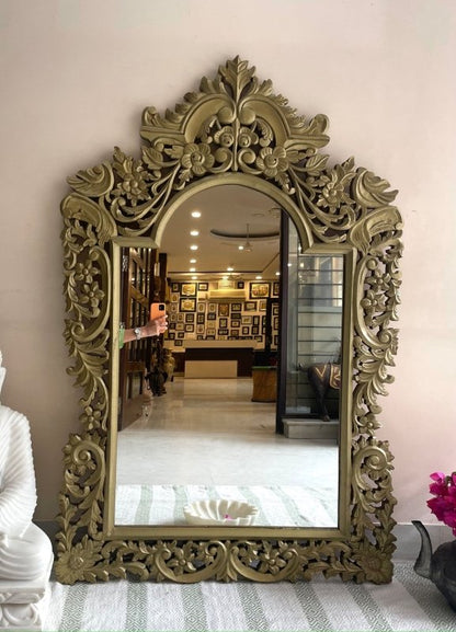 Floral carved wall mirror in gold-toned wood, front view with leafy scrollwork framing a reflected showroom.
