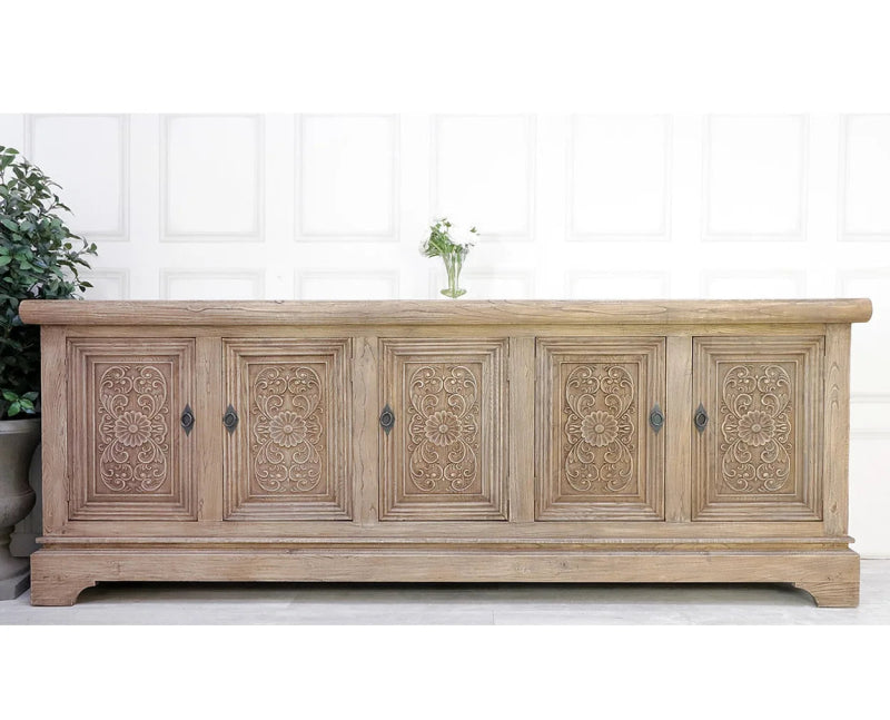 Natural wood sideboard in a detail view showing five recessed doors with matching floral medallions and scrollwork