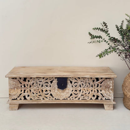 Floral solid wood chest with a rustic finish, front view showing pierced scroll carvings, a black latch and short feet.