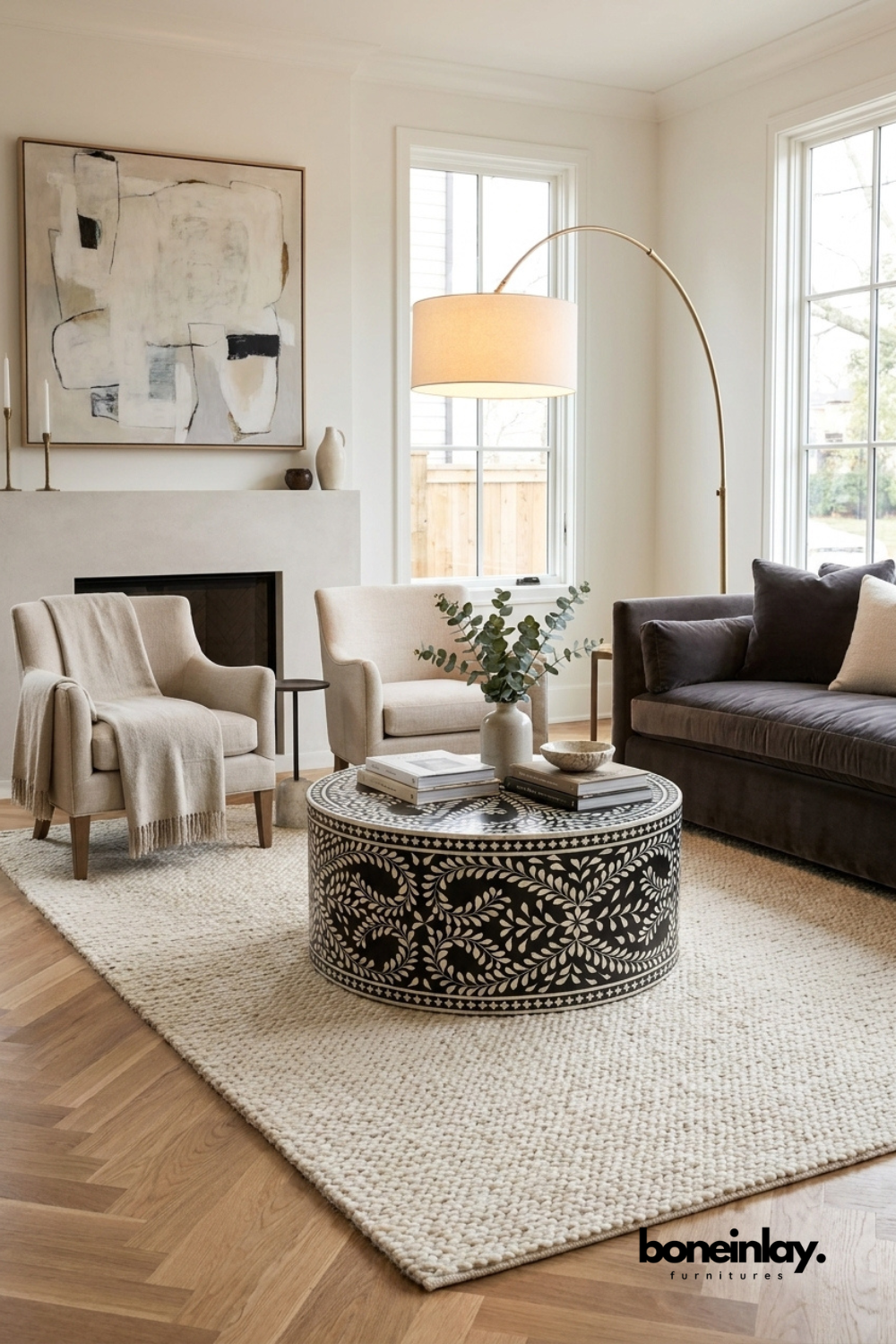 Handcrafted black and white floral bone inlay round drum coffee table styled in a neutral luxury living room with linen sofas, herringbone wood floor, and brass arc lamp.