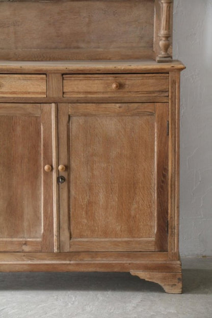 Framed panel wood cabinet in a natural tone, close front view of the lower doors and base against a pale wall.