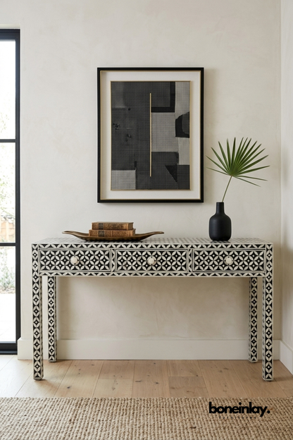 Black and white bone inlay console table featuring a geometric circular pattern across drawers and tapered legs. Complete with round pearl-inspired drawer knobs for a refined finishing touch. Styled with a brass tray, vintage books, and a matte black vase beneath framed wall art. A sophisticated entryway or hallway console with bold graphic appeal.
