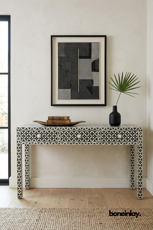 Black and white bone inlay console table featuring a geometric circular pattern across drawers and tapered legs. Complete with round pearl-inspired drawer knobs for a refined finishing touch. Styled with a brass tray, vintage books, and a matte black vase beneath framed wall art. A sophisticated entryway or hallway console with bold graphic appeal.