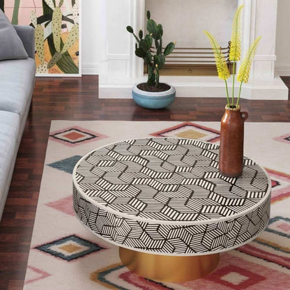Black and white geometric cube bone inlay round coffee table with brass base placed in a contemporary living room with grey sofa and botanical wall art