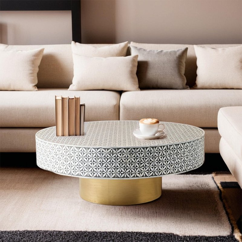 Grey geometric bone inlay drum coffee table with brushed gold pedestal base placed in front of a beige sectional sofa in a luxury living room