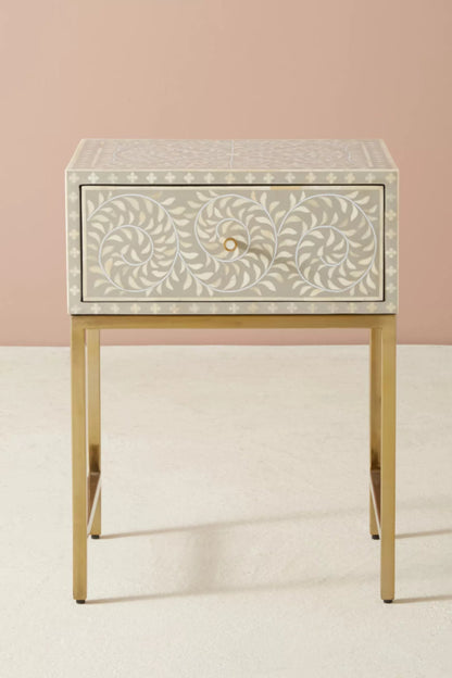 Grey and white bone inlay single drawer nightstand with all-over floral vine leaf pattern, brass metal knob, and slim gold metal frame on a neutral studio background.