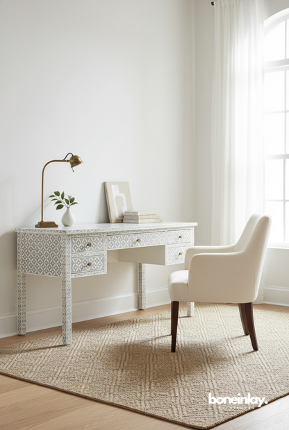 A luxury grey and white geometric bone inlay desk featuring an intricate tile-mosaic pattern across its surface, five drawers, and slender inlaid legs. The desk is accented with minimalist gold-toned knobs and shown in a bright, modern home office setting with a cream-colored armchair. This artisanal workspace piece seamlessly blends traditional Indian craftsmanship with a soft, contemporary Japandi aesthetic.