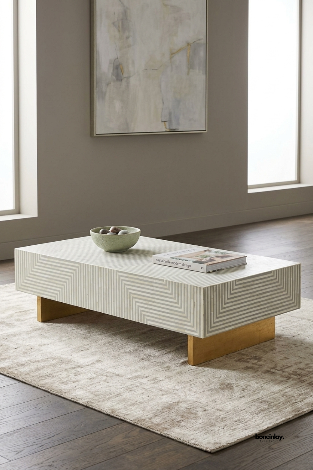 Handcrafted bone inlay rectangular coffee table styled on a plush beige area rug in a sunlit modern living room with abstract wall art. Showcasing a clean low-profile silhouette, geometric line motifs, and lustrous gold finish base supports, this designer center table brings understated luxury and bespoke charm to home interiors.