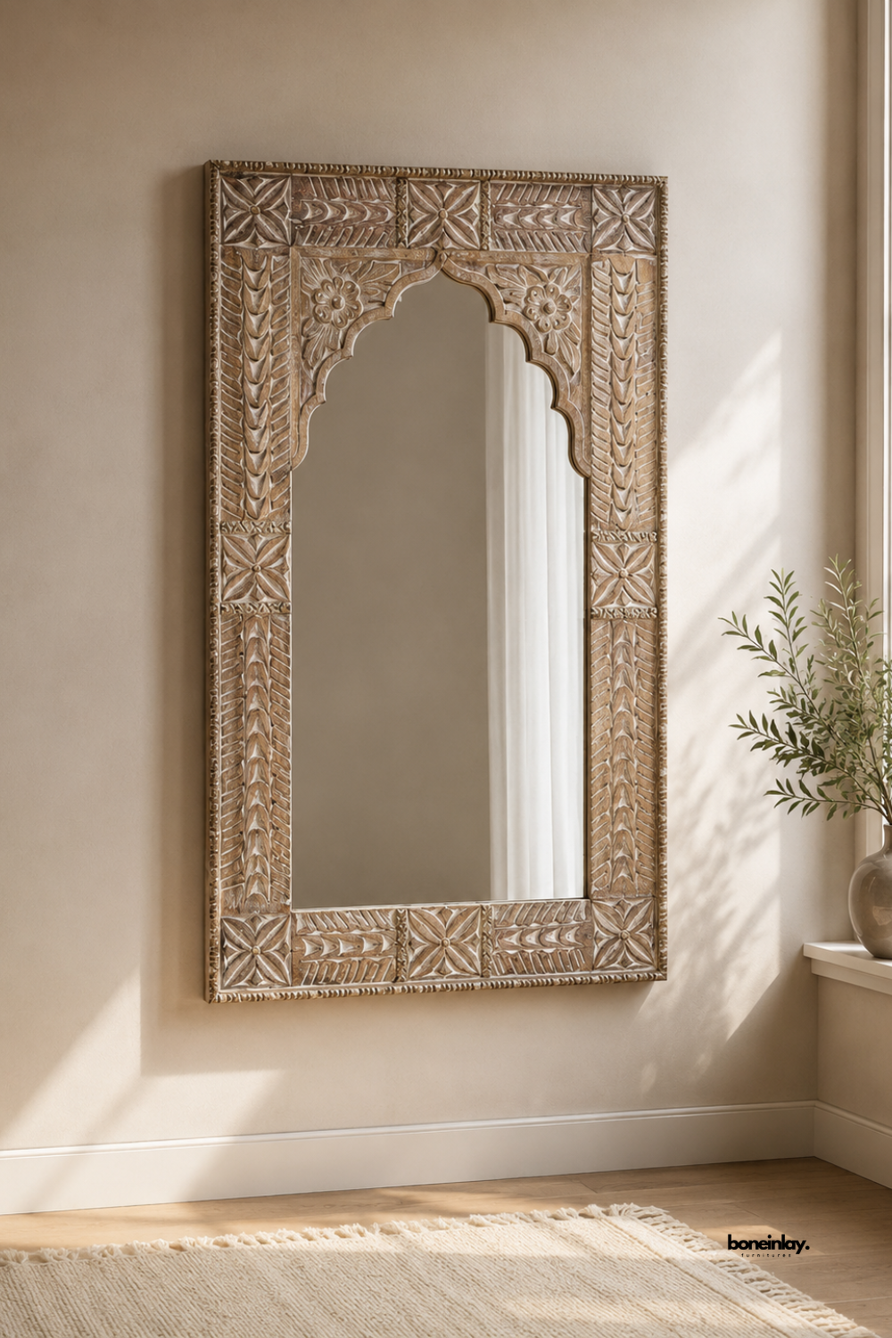 Hand-carved natural wooden wall mirror featuring an Indian scalloped Jharokha arch and detailed floral relief border panels. Styled in a sunlit neutral living room with soft beige walls and a cream rug, this vintage artisan accent mirror adds rustic elegance, depth, and timeless character to luxury interiors.