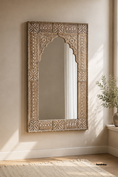 Hand-carved natural wooden wall mirror featuring an Indian scalloped Jharokha arch and detailed floral relief border panels. Styled in a sunlit neutral living room with soft beige walls and a cream rug, this vintage artisan accent mirror adds rustic elegance, depth, and timeless character to luxury interiors.