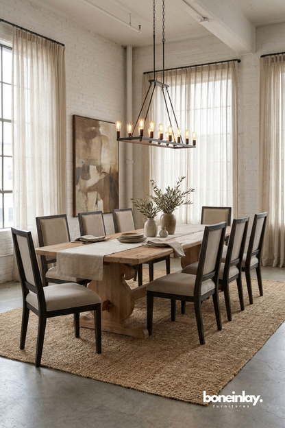 Reclaimed wood trestle dining table with a rustic natural finish.
Solid pedestal trestle base crafted from weathered light wood.
Long rectangular tabletop shows natural grain and knot details.
Styled in an industrial loft dining room with tall curtained windows.