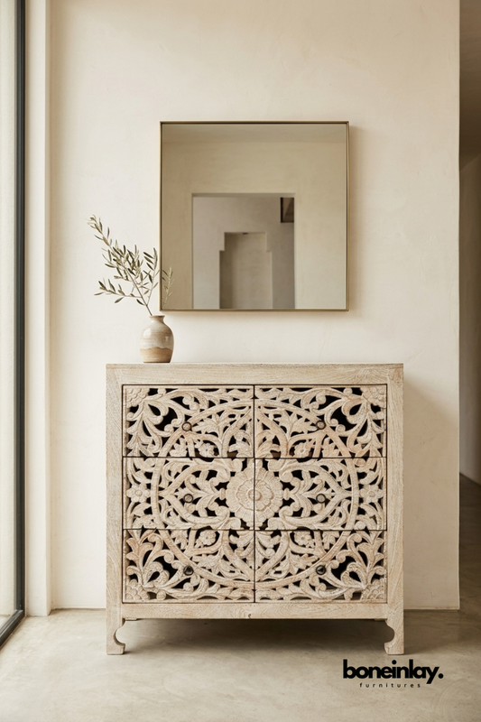 Whitewashed wood chest with an intricate carved floral lattice front.
Symmetrical vine and flower carving spans all six drawer fronts.
Short bracket feet give the piece a slightly raised, grounded stance.
Styled below a square mirror with a stoneware vase on top.