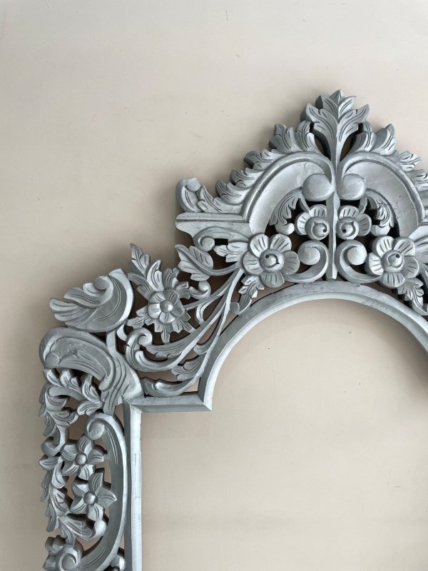 Hand-carved floral mirror frame in silver-finished wood, edge detail view showing the leafy crest and curved trim.