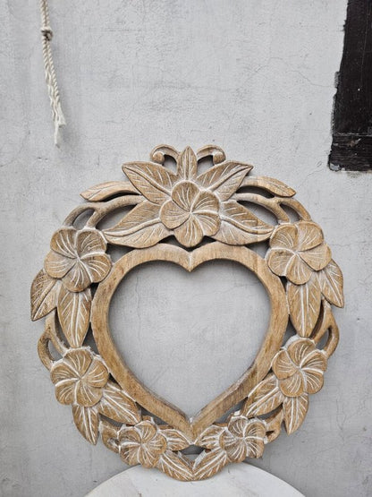 Hand-carved heart wall mirror in rustic solid wood, front view showing an open center surrounded by flowers and leaves.