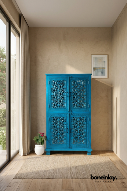 Turquoise hand-carved wood cabinet with an antiqued finish.
Four doors feature intricate carved jaali lattice patterns.
Traditional Indian-inspired craftsmanship in a bold accent color.
Set on a wood block base against a warm plaster wall.