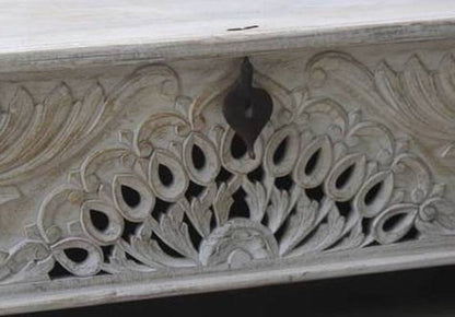 Hand-carved peacock storage coffer in rustic wood, close-up of the pierced feather carving beneath a dark metal latch.