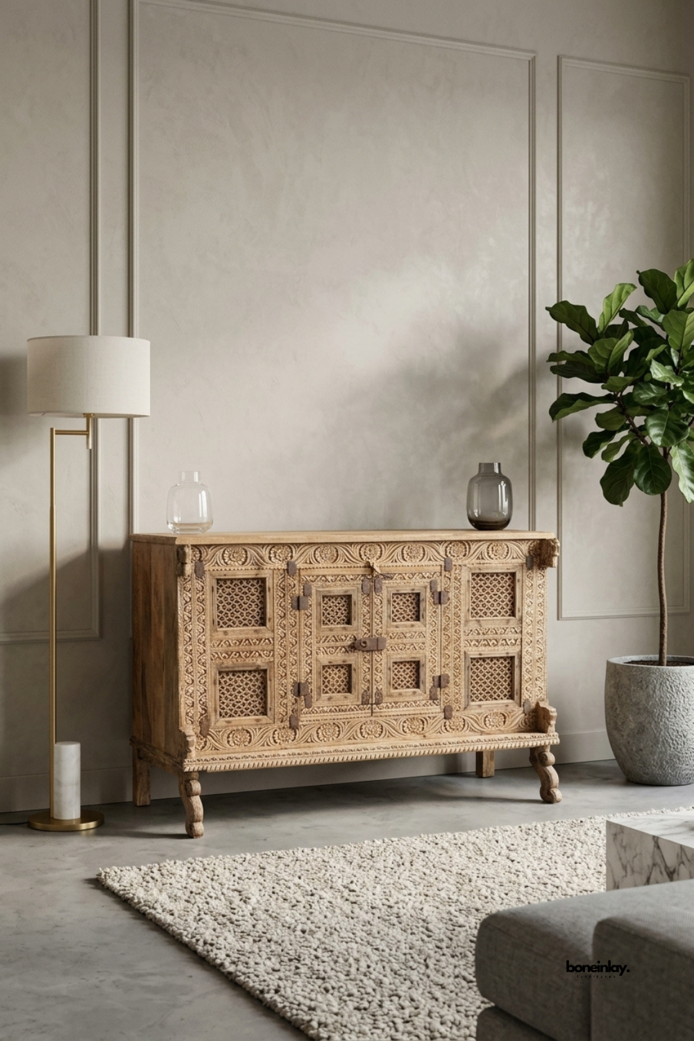 Hand-carved rustic sideboard featuring intricate openwork lattice
door panels, deeply carved floral borders, and vintage iron latch hardware.
Styled in an elegant neutral living space beside a modern brass floor lamp,
this artisan console cabinet brings architectural depth and timeless charm.