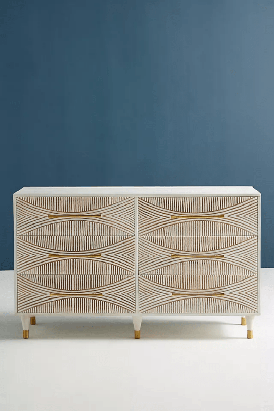 Hand-carved Thalia 6-drawer dresser in white-washed hardwood, front view with brass pulls against a blue wall.