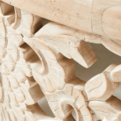 Hand-carved wood cocktail table in a light natural finish, edge detail view showing leaves beneath the top rim.
