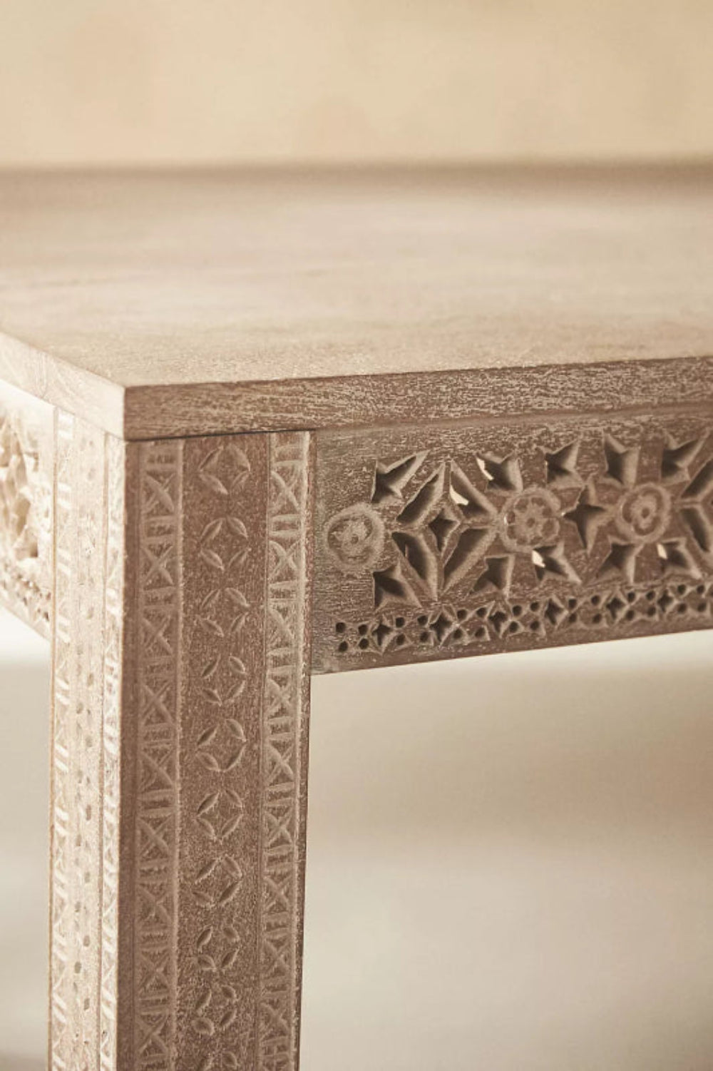 Hand-carved wood dining table, corner detail view showing carved floral edge pattern.